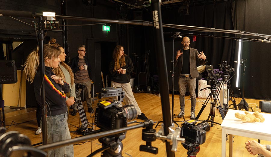 People talking in a dark studio, surrounded by audiovisual equipment