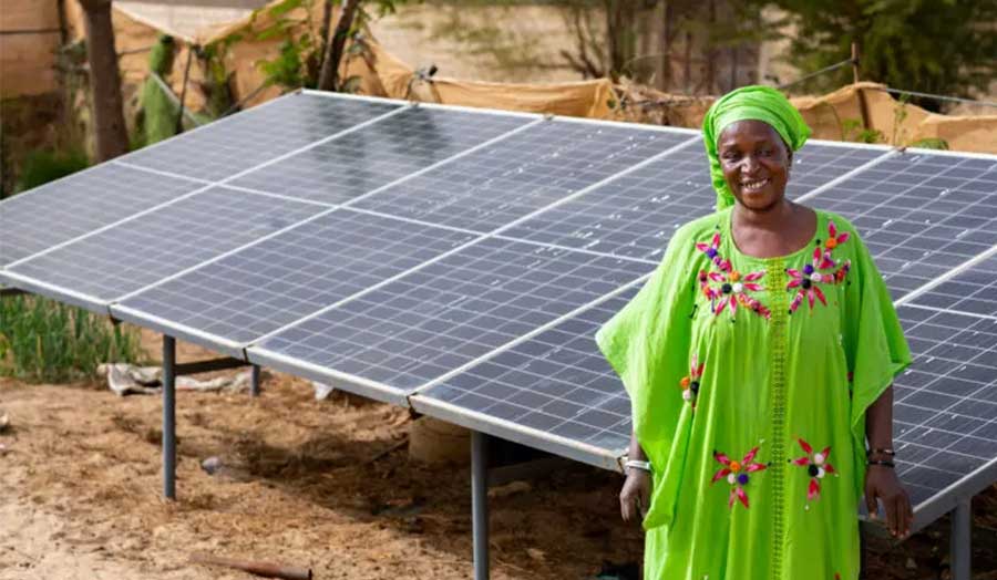 A woman in green clothing stands in front of solar panelling