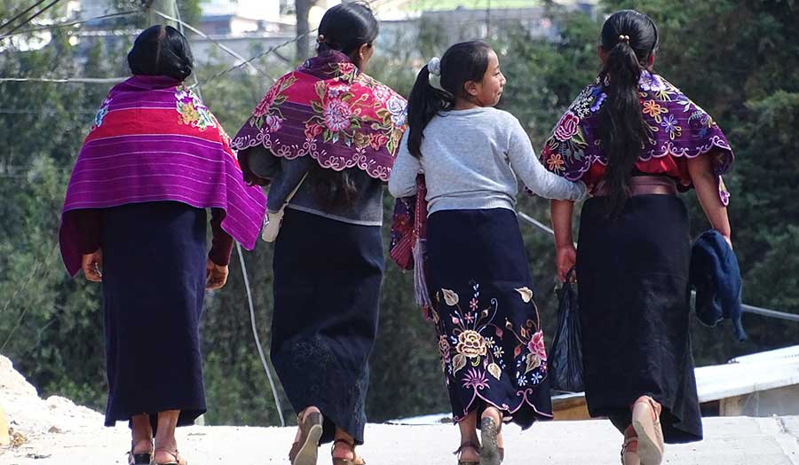 Three Tzotzil women and a girl, with arms linked.