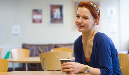 Female student with red hair in a blue dress with a coffee