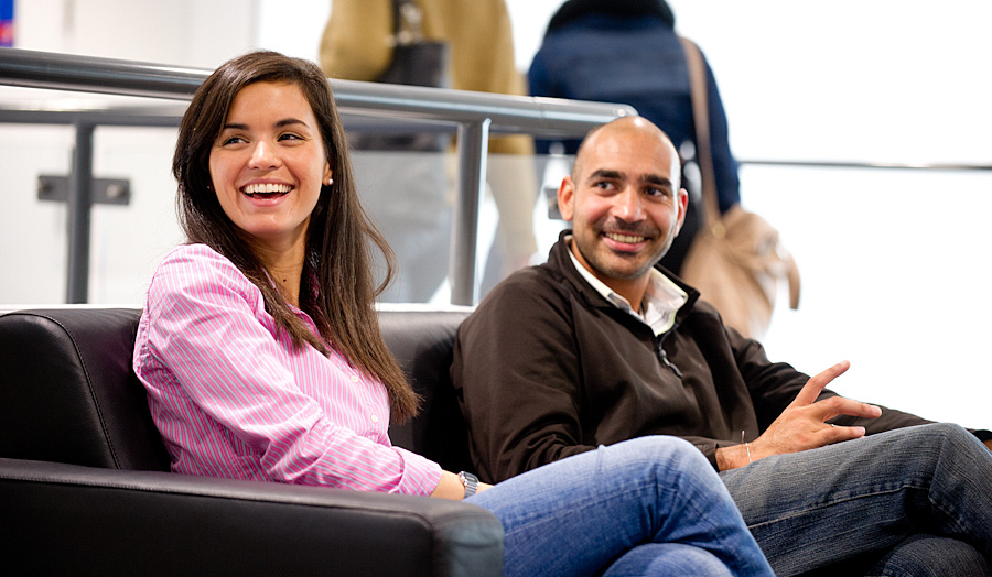 Female and male postgraduate students laughing on sofa, not looking directly at camera