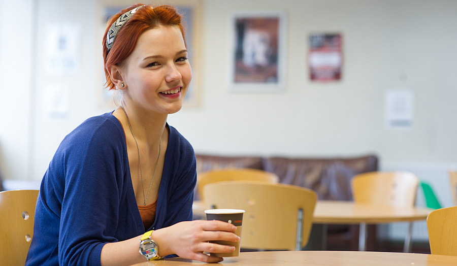 Female student in a blue dress sitting in a cafe smiling