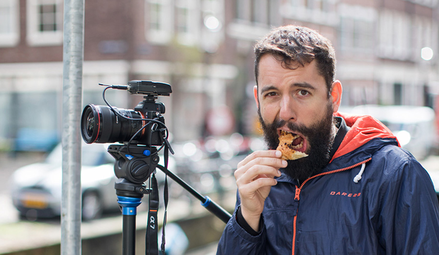Graduate Alejandro eating pizza whilst pictured with his film camera