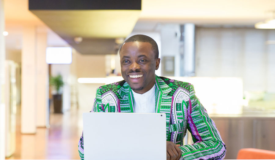 Anthony Boateng on a laptop smiling, wearing a suit jacket with African patterns