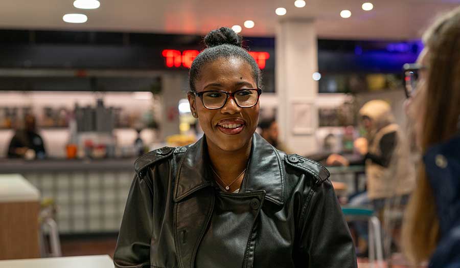 Photo of a student sitting in a cafe smiling.