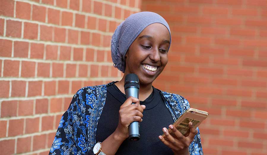 Fatha Hassan, Creative Writing MA student, smiling and holding a microphone