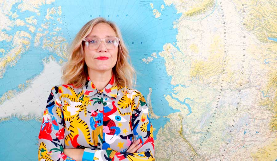 Jenny Theolin standing in front of a map, wearing a contemporary graphic design shirt