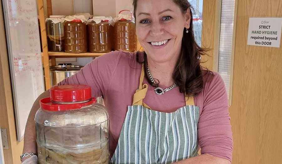 Lou Dillon in an apron holding a large jar of kombucha