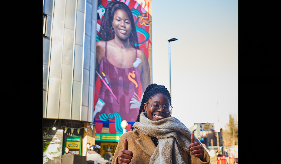 Our graduate Maria Epam standing in front of a mural which is depicting her.