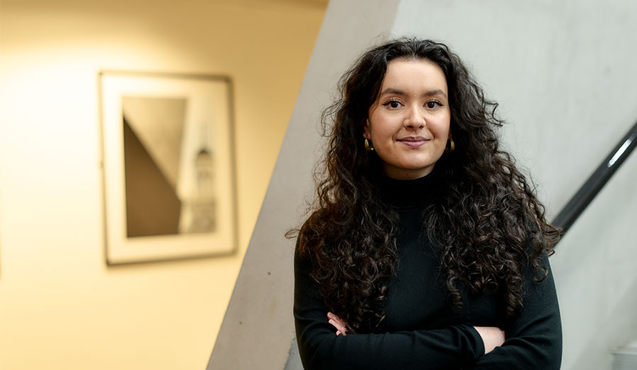 Mia pictured in London Met's graduate centre, smiling with her arms crossed