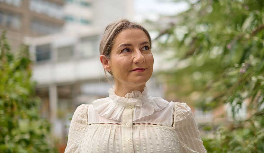 Nicola looking up, wearing a vintage blouse and standing outside with greenery showing