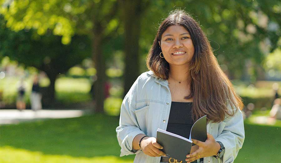 Shirin smiling and holding a book in a park